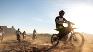 A group of motorcyclists riding on a dusty road with a clear sky.