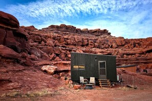 Una pequeña cabaña con puerta y ventanas, rodeada de formaciones rocosas rojas.