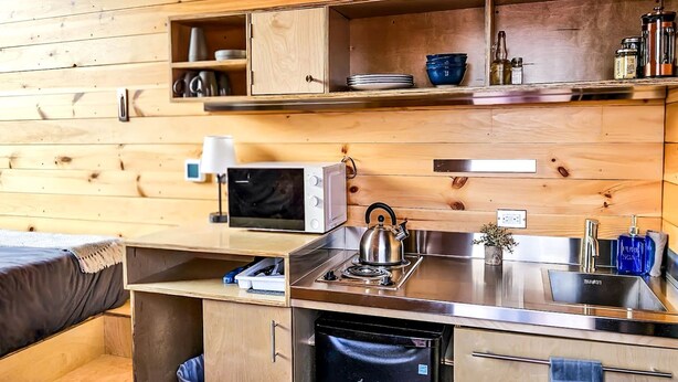 A compact kitchen with a microwave, kettle, sink, and storage cabinets.