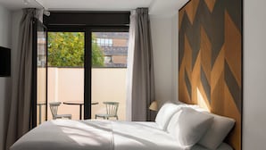 A hotel room with a bed, a small table, two chairs, and a view of the outside. - Limehome Madrid Calle de Bolivia (Madrid)