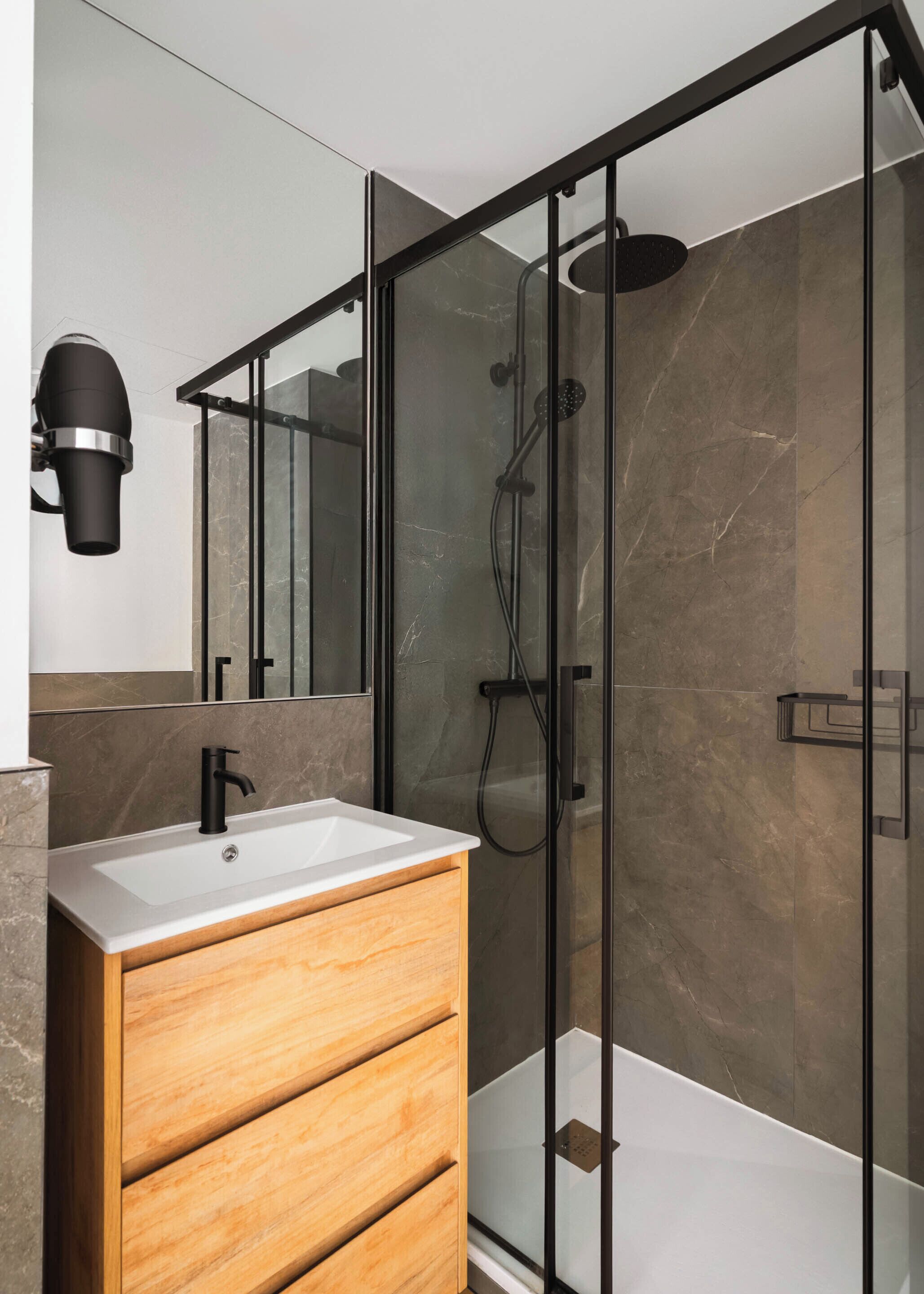A modern bathroom with a wooden vanity, a glass shower enclosure, and a marble-tiled shower wall.