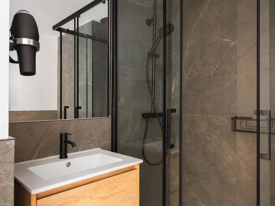 A modern bathroom with a wooden vanity, a glass shower enclosure, and a marble-tiled shower wall.