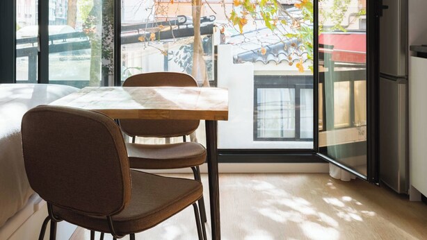 A modern room with a large window, a dining table with chairs, and a refrigerator. - Limehome Madrid Calle de Bolivia (Madrid)