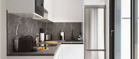 A modern kitchen with a stainless steel refrigerator, a built-in oven, and a marble backsplash.