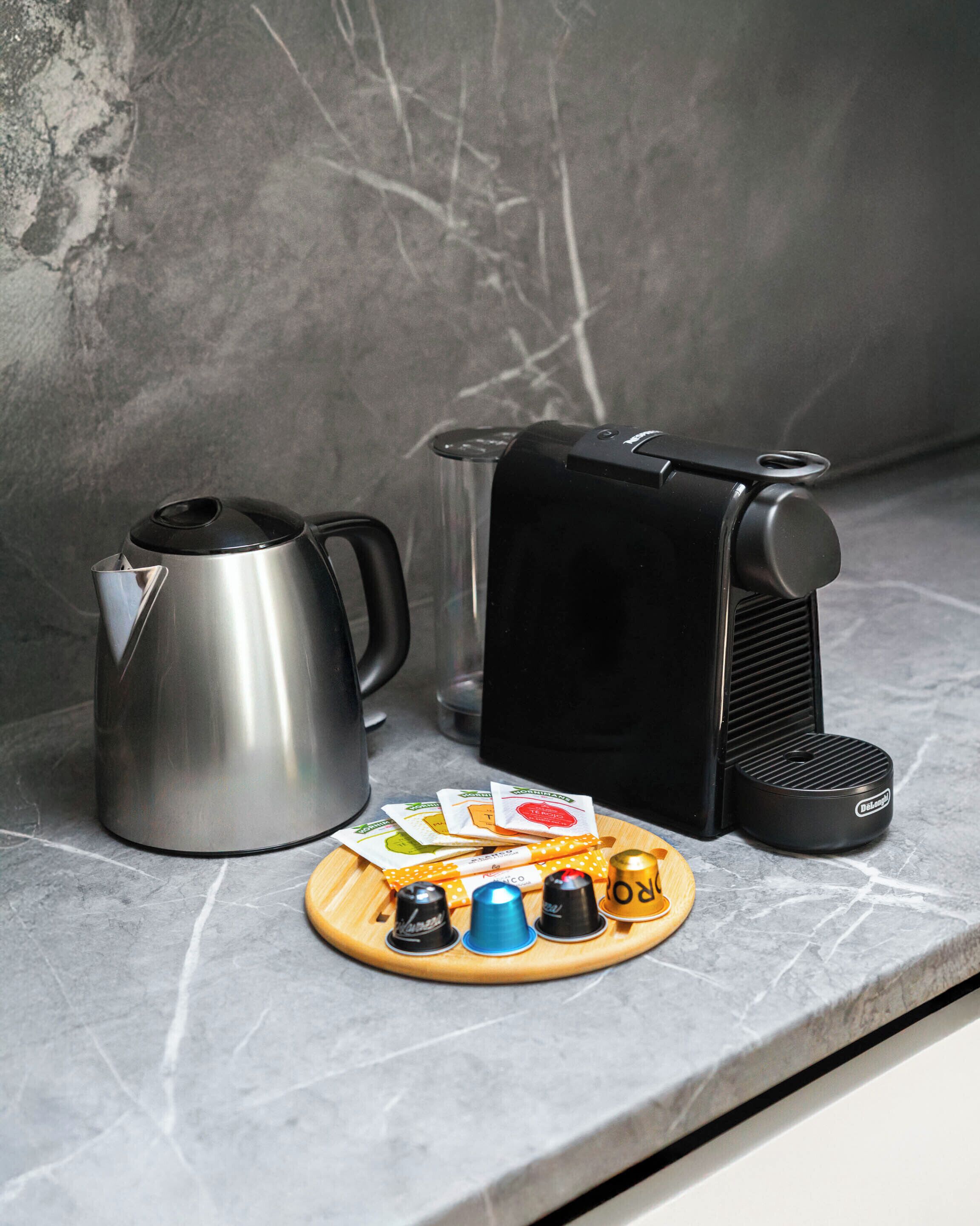 Una encimera de cocina con una cafetera, un hervidor y un soporte para cápsulas de café.