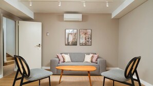 A modern living room with a grey sofa, two black chairs, a wooden coffee table, and two wall-mounted pictures. - Limehome Madrid Calle de Bolivia (Madrid)