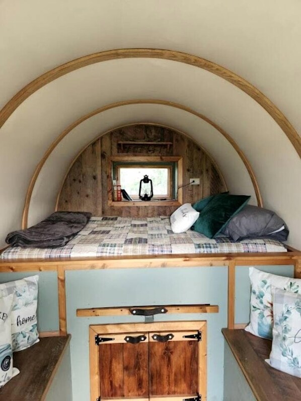 A cozy, rustic room with a wooden bunk bed, a small window with a view, and a wooden cabinet below.