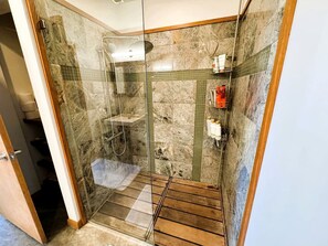 Eine gläserne Dusche mit Holzboden, gefliesten Wänden und Ablage für Toilettenartikel.
