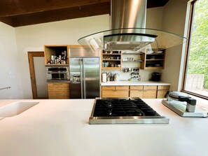 A modern kitchen with a stainless steel range, a glass pendant light, wooden cabinets, and a view through a window. - Gorgeous and Secluded Cabin with Lakefront Views and a Rooftop Terrace, Perfect for a Peaceful Weekend Away (Edgemont)
