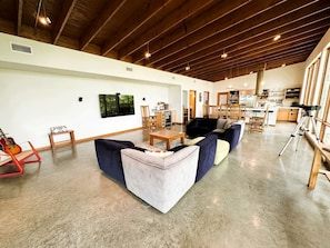 A spacious living area with a high ceiling, a large window, and a kitchen in the background. - Gorgeous and Secluded Cabin with Lakefront Views and a Rooftop Terrace, Perfect for a Peaceful Weekend Away (Edgemont)