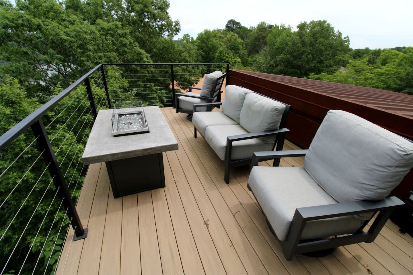 A deck with a table and two sofas, surrounded by a wooden deck and metal railing.