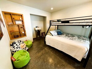 Ein Stockbett mit weißer Decke, ein Regal mit verschiedenen Gegenständen und ein grüner Sitzsack.