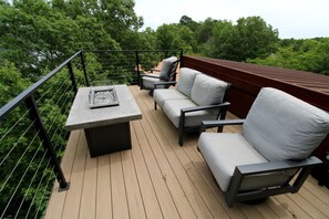 Eine Terrasse mit Tisch und zwei Sofas, umgeben von Holzdeck und Metallgeländer.
