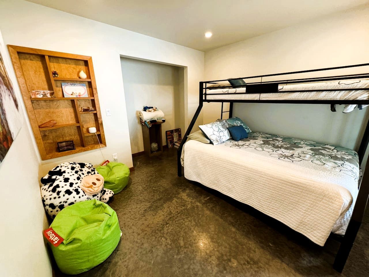 Ein Stockbett mit weißer Decke, ein Regal mit verschiedenen Gegenständen und ein grüner Sitzsack.