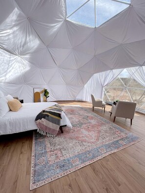 A spacious tented room with a bed, a patterned rug, and a view of the landscape.