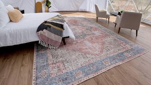 A spacious tented room with a bed, a patterned rug, and a view of the landscape.