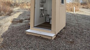 A small, single-room structure with a door, a window, and a built-in sink.