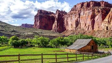A rural landscape with a wooden cabin, green fields, and red rock formations.