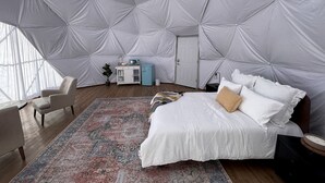A spacious room with a large bed, a small desk, and a chair. - Amazing Dome with Stunning Sights in Wayne County, Utah (Torrey)