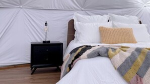 A bedroom with a bed, pillows, a bedside table with a lamp, and a patterned rug. - Amazing Dome with Stunning Sights in Wayne County, Utah (Torrey)