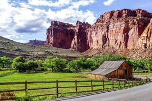 Un paisaje rural con una cabaña de madera, campos verdes y formaciones rocosas de color rojo.