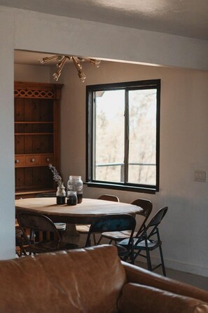 A dining area with a wooden table, chairs, and a window with a view. - Spacious Four Bedroom Cabin on Private Land in Sierra National Forest, Perfect for a Tranquil Weekend in Nature with Family (Dunlap)