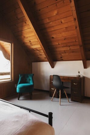 Een kamer met een schuine kap, een bed, een bureau met stoel en een raam.