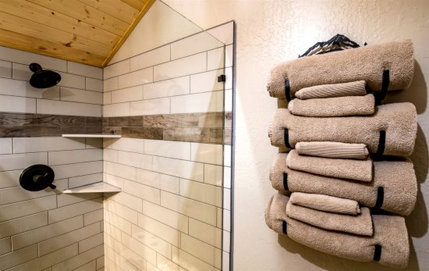 A bathroom with a tiled shower wall, a towel rack with folded towels, and a black shower head.