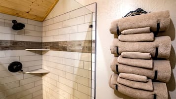A bathroom with a tiled shower wall, a towel rack with folded towels, and a black shower head.