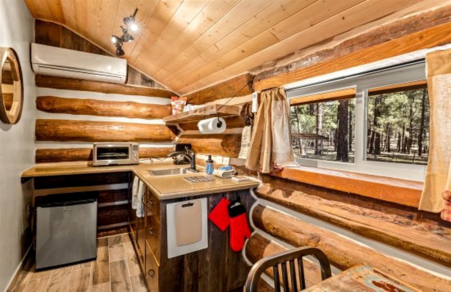 A cabin interior with a kitchenette, a small refrigerator, a microwave, and a window with curtains.