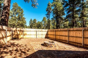 A fenced backyard with a fire pit, surrounded by trees and a clear sky. - Cozy Historic Log Cabin with Fire Pit and Private Backyard on the Edge of the Kaibab National Forest in Parks, Arizona (Parks)