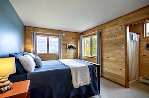 Quarto com cama, mesa de cabeceira, luminária e janela com cortinas.