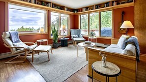 Una sala de estar acogedora con chimenea, un sofá, una butaca y una mesa de centro. Se observan estanterías y un ventanal grande.