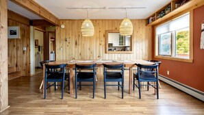 Una habitación con paneles de madera, una mesa de comedor, sillas, lámparas colgantes y un ventanal grande.