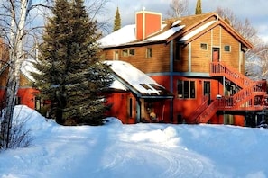 Uma cabana de madeira com fachada vermelha, uma escadaria e um telhado coberto de neve.