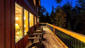 Una terraza de madera con mobiliario exterior, barandilla y un edificio con ventanas.
