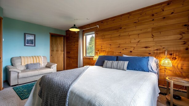 Un dormitorio con cama, sofá, ventana con vistas y pared de madera.