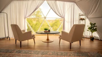 Une tente avec deux chaises placées face à une table, un tapis et une plante.