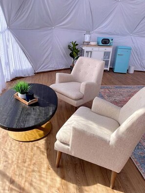 Une pièce aménagée comme une tente, avec une table ronde, deux fauteuils, un petit meuble et une plante.