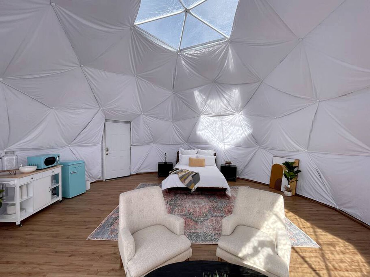 A tented room with a bed, two armchairs, a small table, and a microwave.