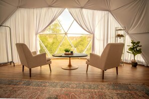 Une tente avec deux chaises placées face à une table, un tapis et une plante.