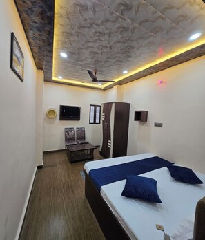 A hotel room with a bed, a wardrobe, a desk, a chair, a television, and a ceiling fan. - Kashika Guest House - near Main Places (Varanasi)