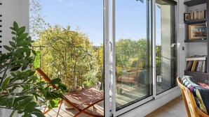 Ein Balkon mit einer Schiebetür aus Glas, einem Holzstuhl und einem Bücherregal mit Büchern und gerahmten Bildern.