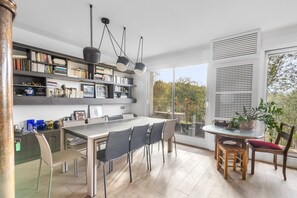 Un espace repas moderne avec une grande table, des chaises et une bibliothèque remplie de livres et d’objets décoratifs.
