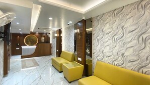 A modern lobby with marble flooring, yellow sofas, and a reception desk with a circular decorative element. - Shree Shanteshwar Mahadev Inn (Varanasi)