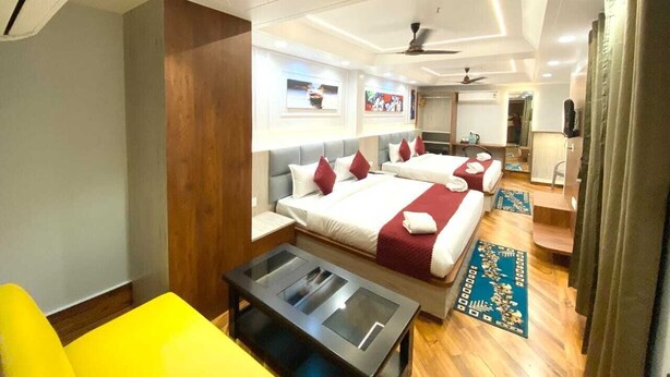 A hotel room with two beds, a small table, a chair, a mirror, and a ceiling fan. - Shree Shanteshwar Mahadev Inn (Varanasi)