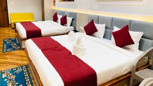 A hotel room with two beds, each with white bedding and red accents, a bright yellow bench, and artwork depicting a temple and boats on the walls. - Shree Shanteshwar Mahadev Inn (Varanasi)