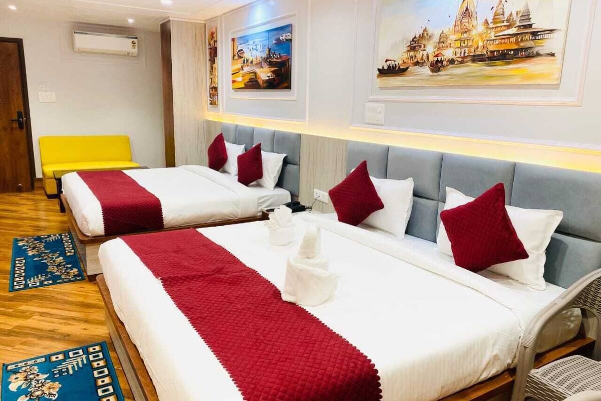 A hotel room with two beds, each with white bedding and red accents, a bright yellow bench, and artwork depicting a temple and boats on the walls.