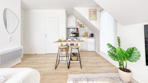 Une cuisine moderne et bien éclairée, avec un coin repas, une grande plante et un escalier menant à l’étage supérieur.