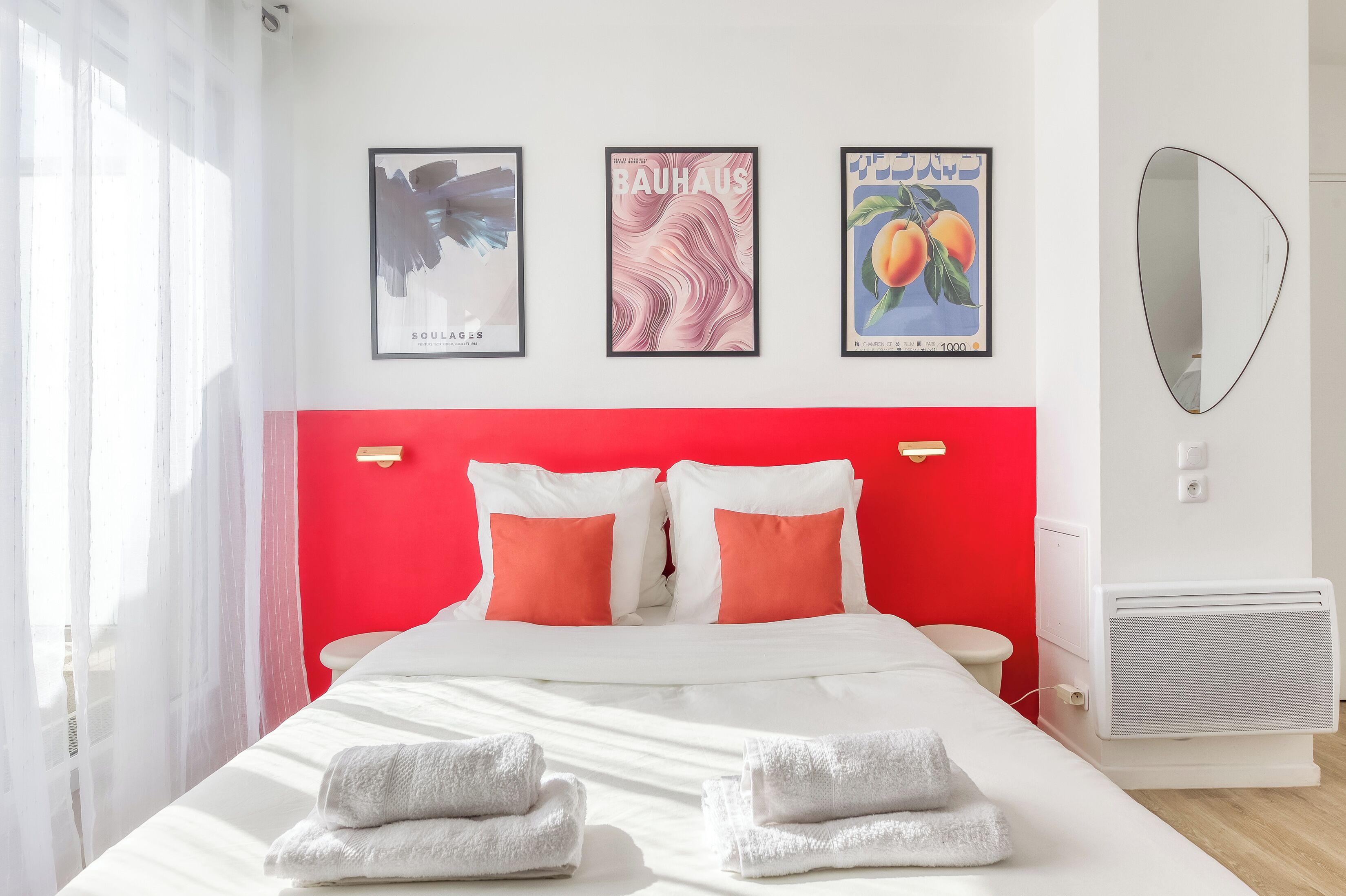 A hotel room with a red headboard, white bedding, and three framed artworks on the wall.